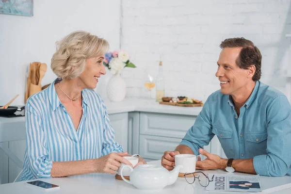 Happy senior couple smiling each other and talking while drinking tea together at home — Stock Photo