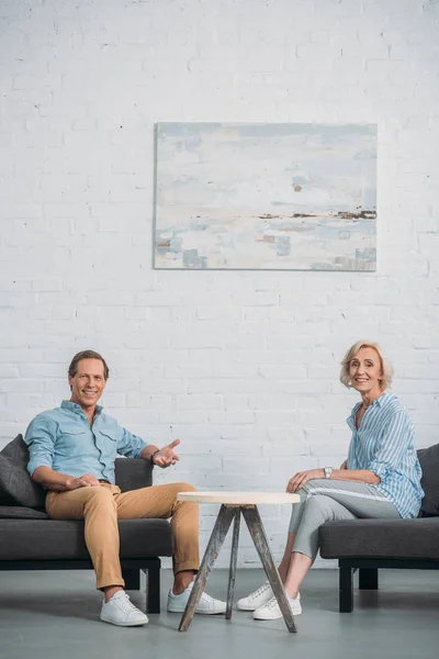 Feliz pareja de ancianos sonriendo a la cámara mientras están sentados juntos en casa - foto de stock