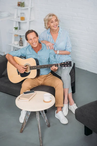 Вид под высоким углом на счастливую пожилую пару, играющую дома на гитаре — стоковое фото