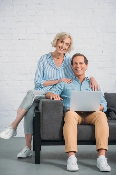Feliz pareja de ancianos utilizando el ordenador portátil y sonriendo a la cámara - foto de stock