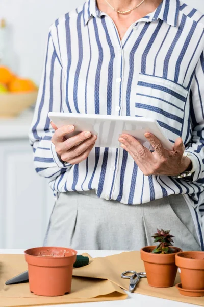 Schnappschuss von Seniorin mit digitalem Tablet beim Pflanzen-Anbau zu Hause — Stockfoto