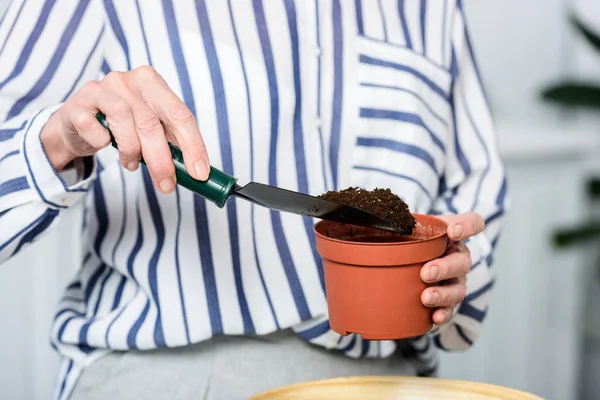 Tiro recortado de mujer mayor sosteniendo pala pequeña y olla con tierra - foto de stock