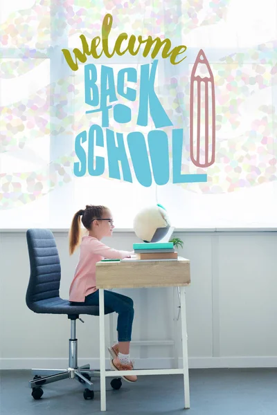 Pequeña colegiala que estudia con libros y portátil en casa con bienvenida de nuevo a las letras de la escuela y lápiz ilustración - foto de stock