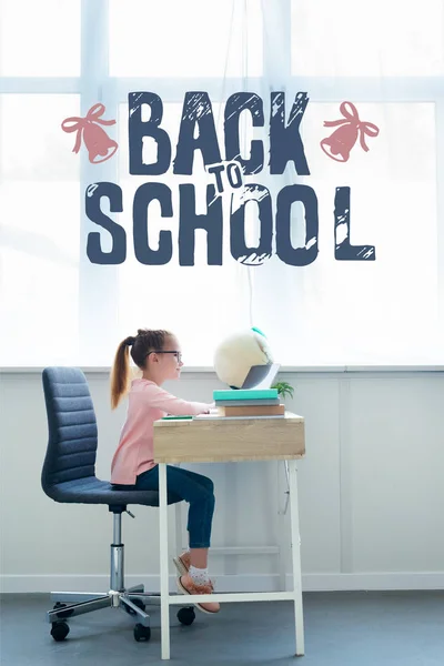 Side view of little schoolgirl studying with books and laptop at home with 