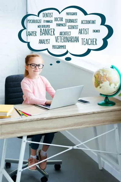 High angle view of child in eyeglasses smiling at camera while using laptop and studying at home with words of different professions in speech bubble — Stock Photo