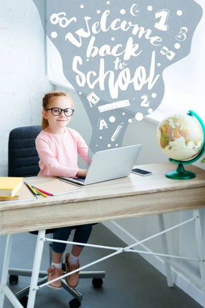High angle view of child in eyeglasses smiling at camera while using laptop with icons and welcome back to school concept — Stock Photo