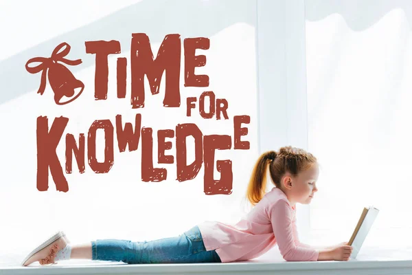 Adorable little schoolgirl reading book and lying on windowsill with 