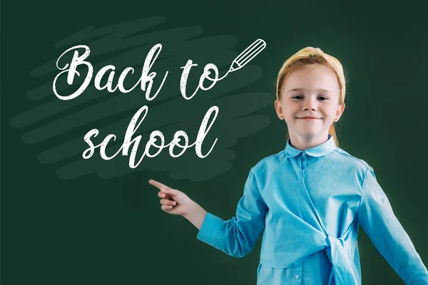 Belle écolière aux cheveux roux pointant vers le tableau noir avec lettrage de retour à l'école — Photo de stock
