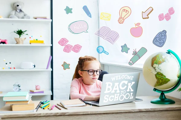 Beautiful child in eyeglasses using laptop while studying at desk at home, welcome back to school — Stock Photo