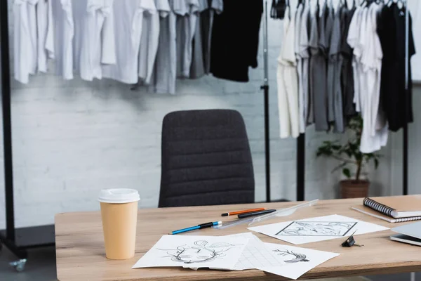 Selective focus of coffee cup and paintings on working table in clothing design studio — Stock Photo