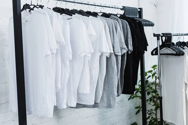 Selective focus of white, black and grey empty t-shirts on hangers in clothing design studio — Stock Photo