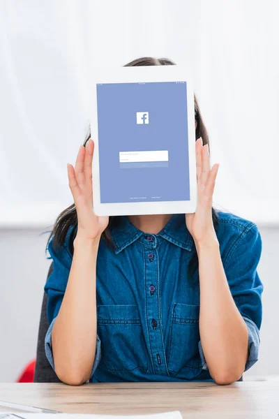 Junge Frau verdeckt Gesicht mit digitalem Tablet mit Facebook-Website auf dem Bildschirm — Stockfoto