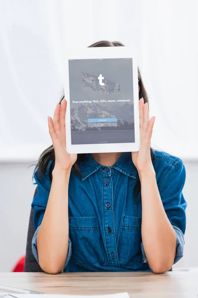 Mujer joven cubriendo cara por tableta digital con sitio web tumblr en la pantalla - foto de stock