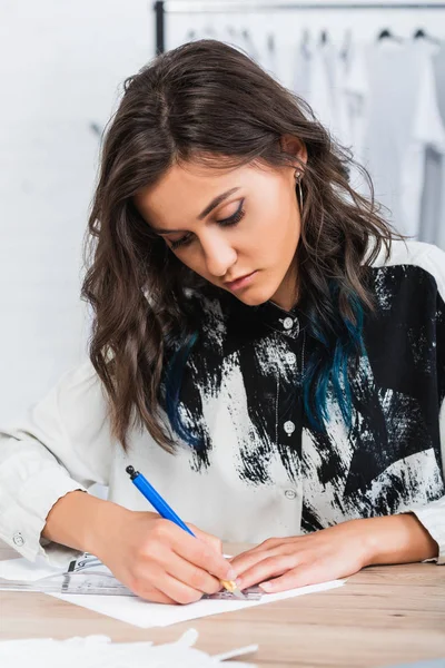 Mujer diseñadora de moda pintura en mesa de trabajo en estudio de diseño de ropa - foto de stock