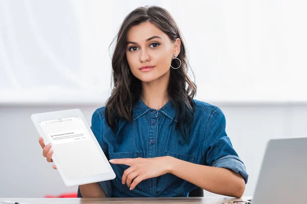 Attractive young woman pointing on digital tablet screen with blocked vk.com website — Stock Photo