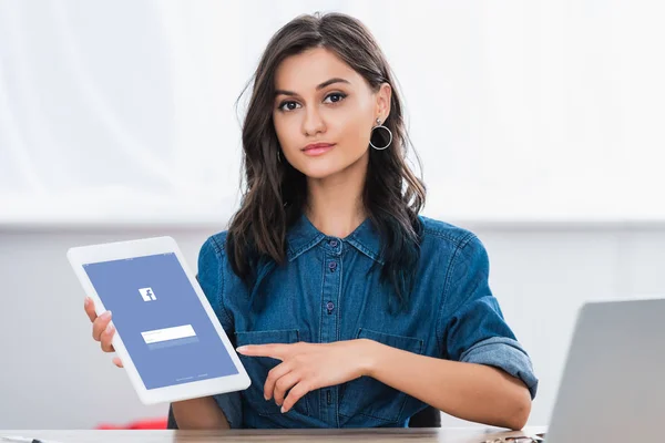 Atractiva mujer joven apuntando en la pantalla de tableta digital con el sitio web de facebook - foto de stock