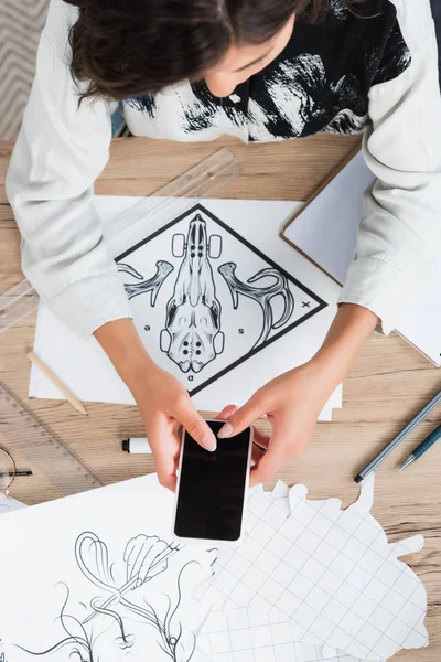 Overhead view of female fashion designer taking picture of painting for print on t-shirt at table — Stock Photo