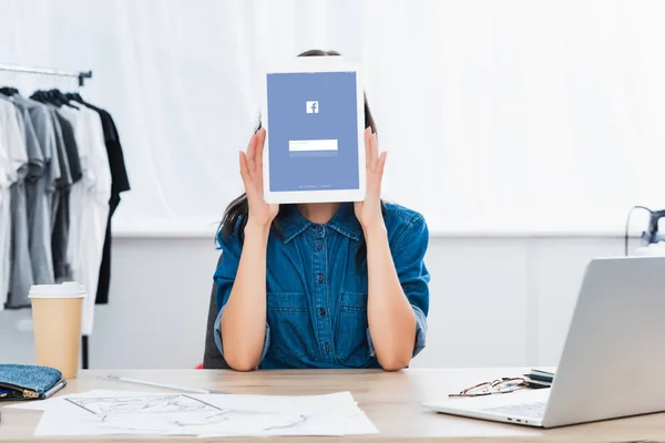 Mujer joven cubriendo cara por tableta digital con el sitio web de facebook en pantalla - foto de stock