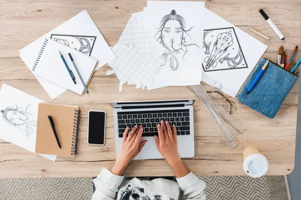 Обрезанное изображение женщины-дизайнера с помощью ноутбука за столом с картинами и смартфоном — стоковое фото