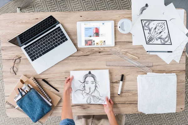 Imagen recortada del diseñador femenino poniendo pintura en la mesa con el ordenador portátil y la tableta digital con ebay en la pantalla - foto de stock