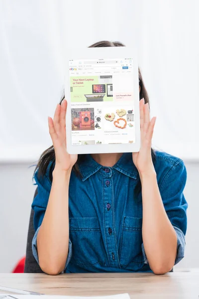 Mujer joven cubriendo cara por tableta digital con el sitio web de ebay en la pantalla - foto de stock