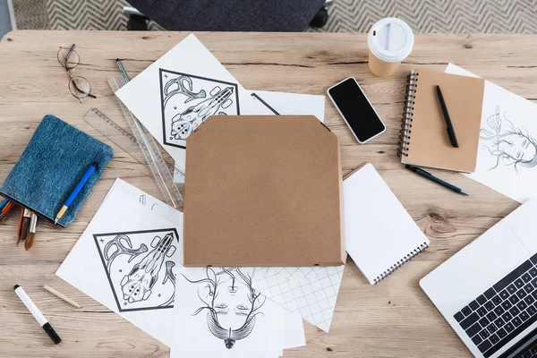 Vue du dessus de la boîte à pizza, peintures, smartphone avec écran vierge et ordinateur portable sur la table de travail — Photo de stock