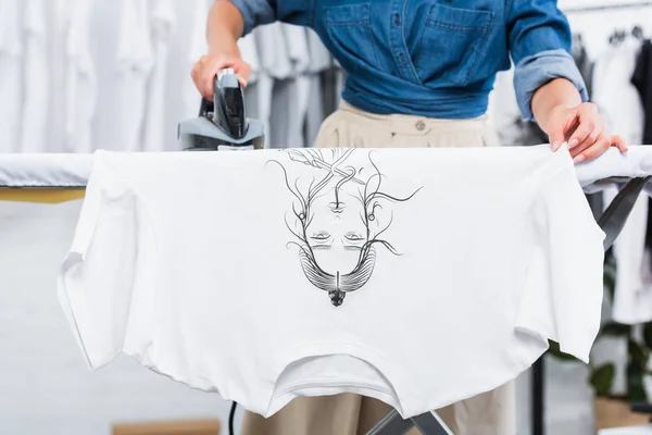 Immagine ritagliata di donna designer stiratura t-shirt con stampa in studio di design di abbigliamento — Foto stock