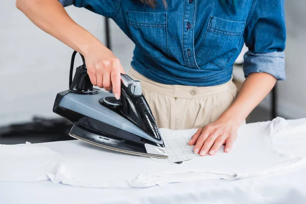 Cropped image of young woman ironing t-shirt at home — Stock Photo