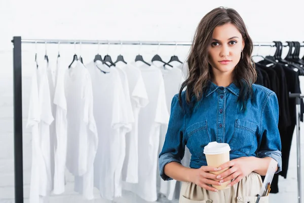 Joven diseñadora de moda sosteniendo taza de café en estudio de diseño de ropa - foto de stock