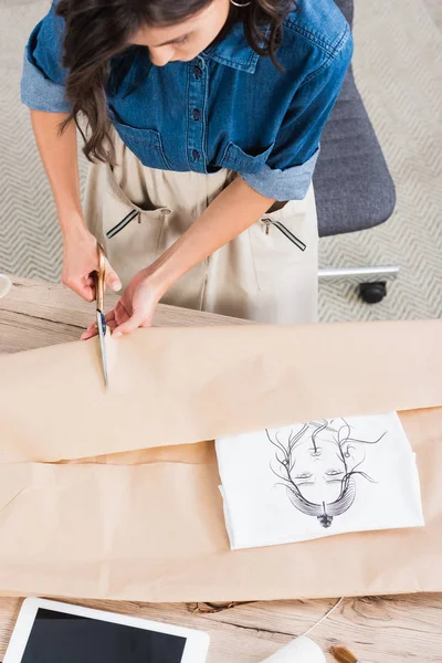 Vista aérea do designer de moda feminina que embrulha t-shirt com impressão em pacote de papel à mesa — Fotografia de Stock