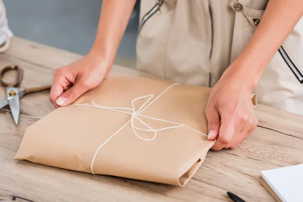 Cropped image of female fashion designer wrapping paper package at table — Stock Photo