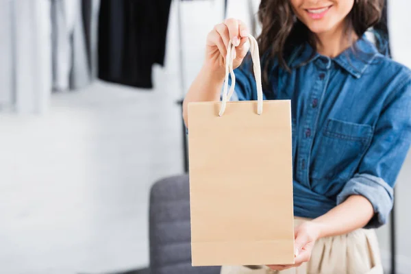 Imagen recortada de mujer sonriente agujero bolsa de papel en estudio de diseño de ropa - foto de stock