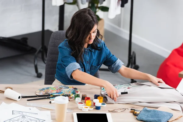 Жіночий дизайнер моди, що працює за столом з чашкою кави та цифровим планшетом у студії дизайну одягу — стокове фото