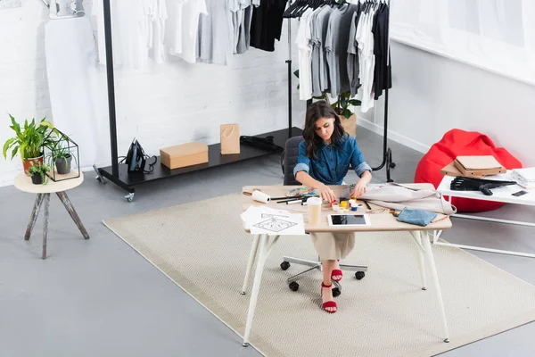 Vista de ángulo alto de la pintura del diseñador de moda femenino en la chaqueta en la mesa de trabajo en el estudio de diseño de ropa - foto de stock