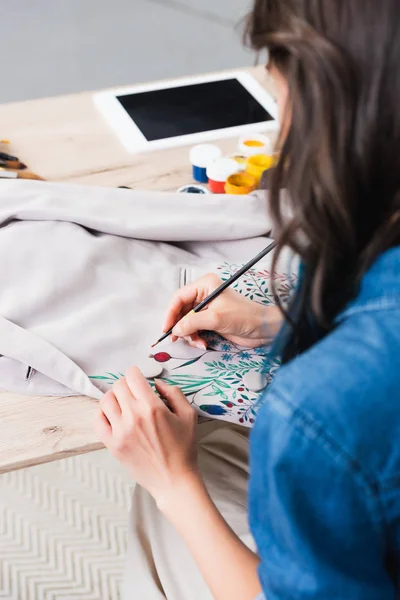 Mujer diseñadora de moda pintura sobre chaqueta en mesa de trabajo en estudio de diseño de ropa - foto de stock