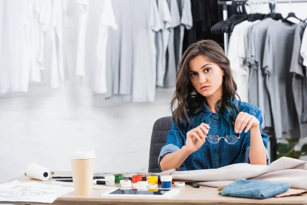 Young female fashion designer sitting at working table with paints an coffee — Stock Photo