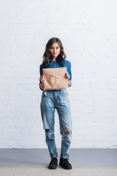 Приваблива молода жінка тримає паперовий пакет перед цегляною стіною — стокове фото