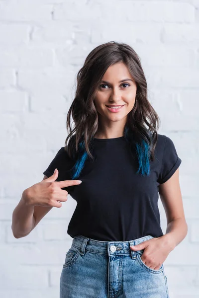 Щаслива молода жінка вказує пальцем на порожню чорну футболку — стокове фото