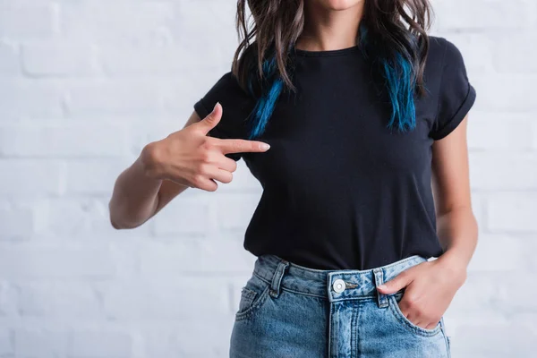 Image recadrée d'une jeune femme pointant du doigt sur un t-shirt noir vide — Photo de stock