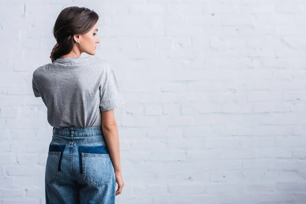 Side view of young woman showing empty back of grey t-shirt in front of brick wall — Stock Photo