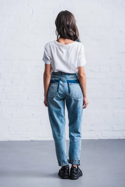 Vue arrière de la jeune femme en t-shirt blanc vide devant un mur de briques — Photo de stock