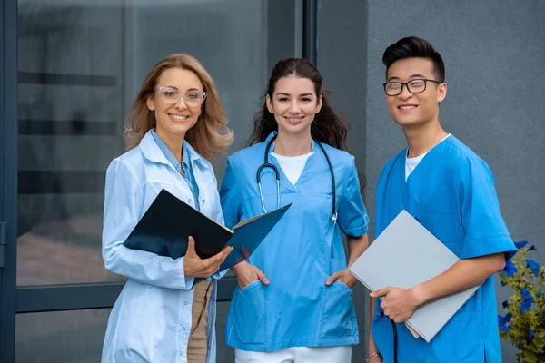 Lächelnder Lehrer mit zwei multikulturellen Studenten, die an der medizinischen Universität in die Kamera schauen — Stockfoto
