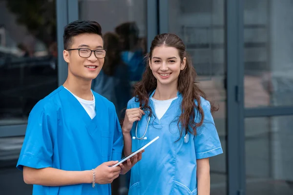 Multikulturelle Medizinstudenten halten Tablet in der Hand und blicken in die Kamera der Medizinischen Universität — Stockfoto