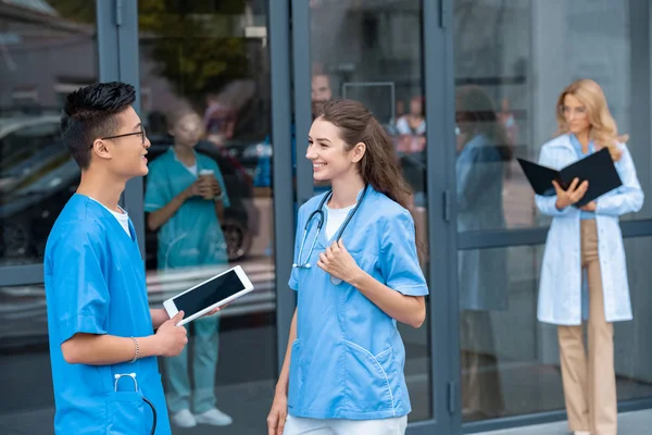 Мультикультурные студенты смотрят друг на друга и держат планшет в медицинском университете — стоковое фото