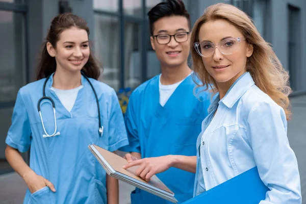 Teacher looking at camera and standing with multicultural students at medical university — Stock Photo