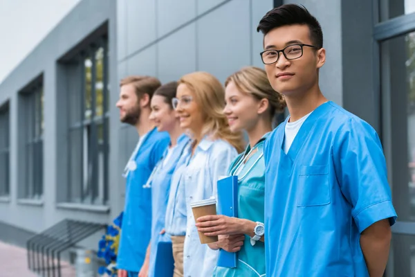 Teacher with multicultural students standing in row near medical university, asian man looking at camera — Stock Photo