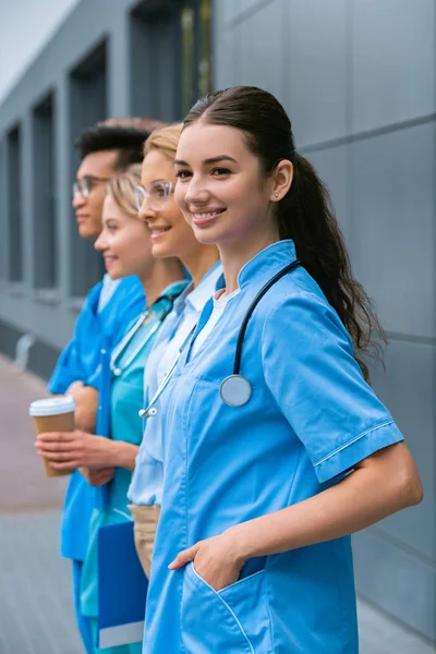 Side view of teacher and happy multicultural students standing in row near medical university — Stock Photo