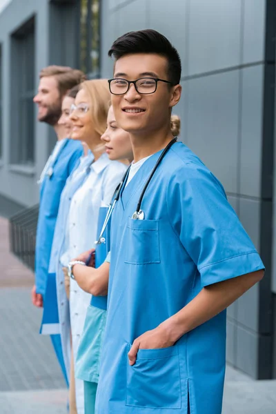 Teacher with multicultural students standing in row near medical university, asian man looking at camera — Stock Photo