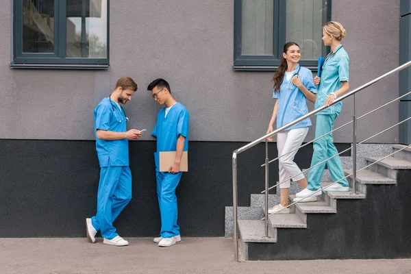 Мультикультурные студенты-медики смотрят на смартфон возле медицинского университета — стоковое фото