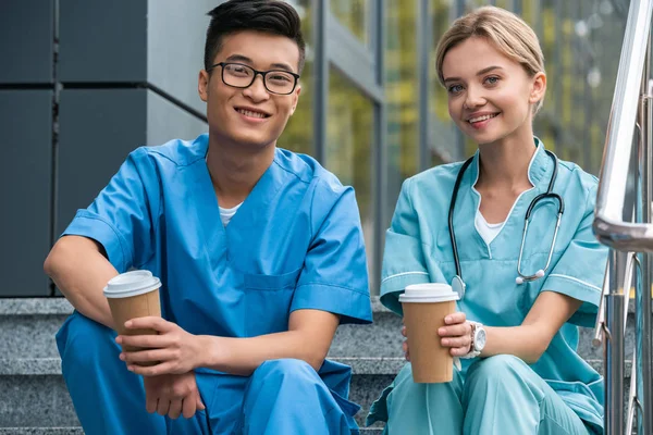 Multikulturelle Medizinstudenten sitzen mit Kaffee in Pappbechern auf der Treppe — Stockfoto